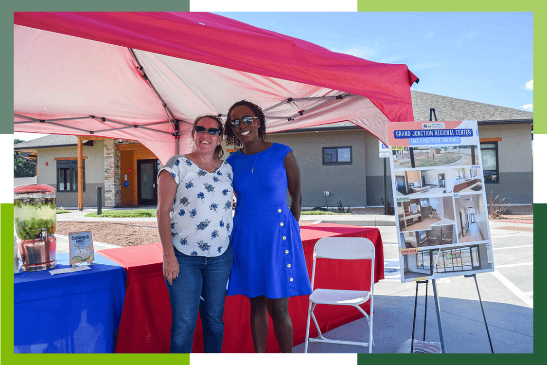 Two female Grand Junction Regional Center staff members smile during an outdoor open house event