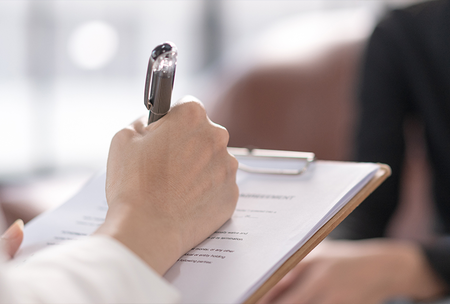 Photograph of woman writing on a clipboard while speaking to a man