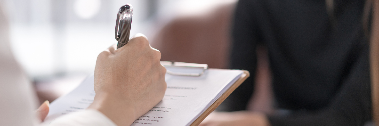 Person with clipboard taking notes while facing another person